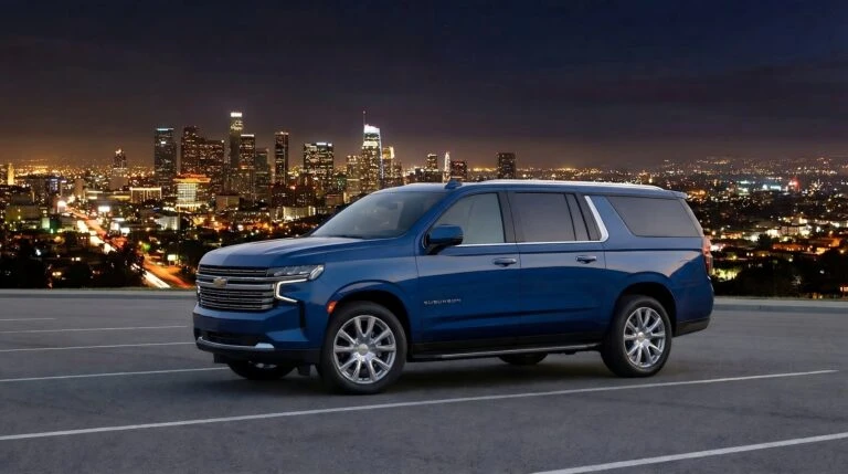 Camioneta blindada tipo Suburban color azul estacionada en mirador con vista panorámica de una ciudad iluminada de noche, unidad lista para operación de movilidad segura de Shel-Ha Soluciones.
